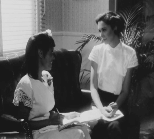 Black and white photo of two women sitting on a couch facing each other