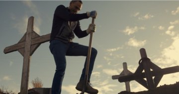 A man hits the ground with a shovel, surrounded by crosses